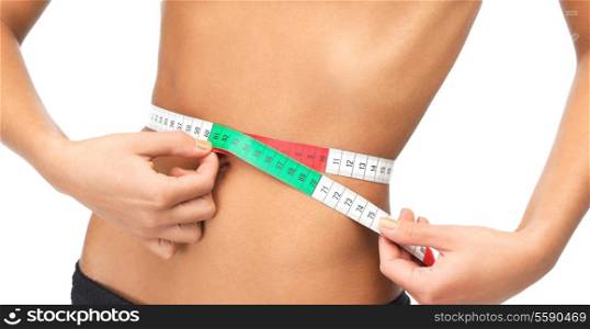 health, dieting and fitness concept - close up of woman measuring her waist with measuring tape