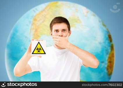 health, epidemic and pandemic concept - scared young man with biohazard caution sign over earth planet on background. scared man with biohazard sign over earth planet