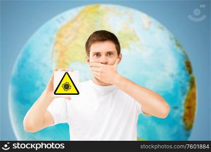 health, epidemic and pandemic concept - scared young man with coronavirus caution sign over earth planet on background. scared man with coronavirus sign over earth planet