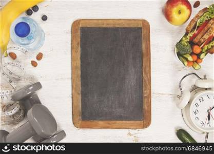 Health & Fitness Food in lunch box, measuring tape, dumbbells and alarm clock on wooden board.