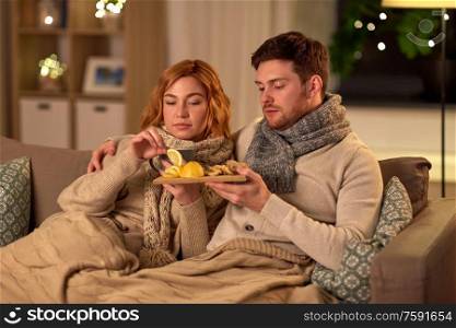health, flu and people concept - sick young couple in scarves drinking tea with lemon and ginger at home. sick young couple drinking tea with lemon at home
