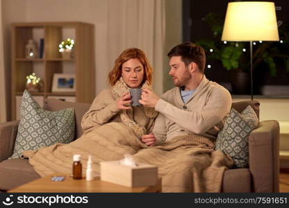 health, flu and people concept - sick young couple in scarves drinking hot tea at home. sick young couple drinking hot tea at home