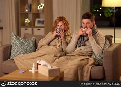 health, flu and people concept - sick young couple in scarves drinking hot tea at home. sick young couple drinking hot tea at home