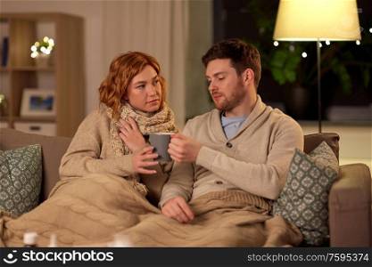 health, flu and people concept - sick young couple in scarves drinking hot tea at home. sick young couple drinking hot tea at home