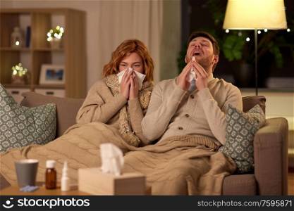 health, flu and people concept - sick young couple with tissue blowing nose and sneezing at home. sick young couple with tissue blowing nose at home