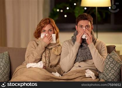 health, flu and people concept - sick young couple with tissue blowing nose at home. sick young couple with tissue blowing nose at home