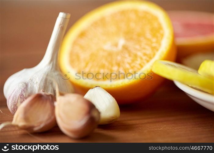 health, food, cooking, traditional medicine and ethnoscience concept - close up of garlic and orange on wooden table