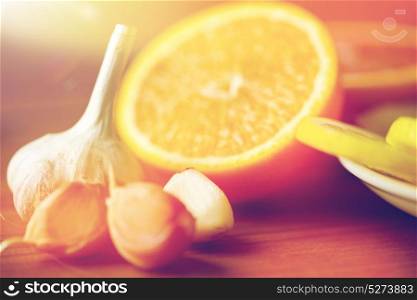 health, food, cooking, traditional medicine and ethnoscience concept - close up of garlic and orange on wooden table. close up of garlic and orange on wooden table