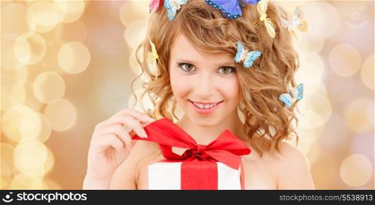 health, holidays and beauty concept - happy teenage girl with butterflies in hair opening gift box