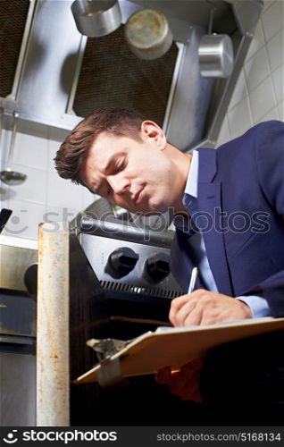 Health Inspector Looking At Oven In Commercial Kitchen