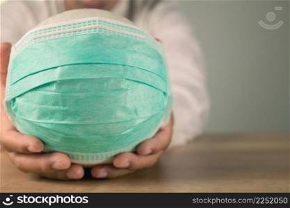 Health insurance in COVID concept. A man holds a white ball with green medical mask. Medium close up shot with copy space.