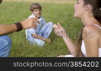 Health issues and young people, child looking at man and woman smoking cigarette and talking in park. Rack focus