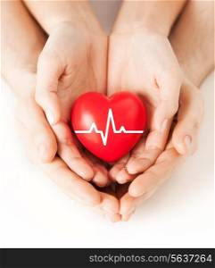 health, medicine and charity concept - closeup of couple hands holding red heart with ecg line
