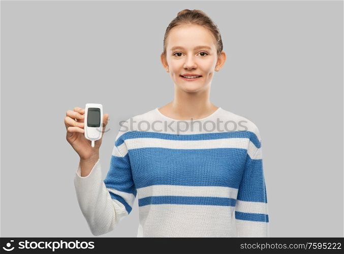 health, medicine and diabetic concept - happy smiling teenage girl with glucometer over grey background. happy smiling teenage girl with glucometer