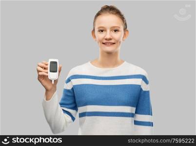 health, medicine and diabetic concept - happy smiling teenage girl with glucometer over grey background. happy smiling teenage girl with glucometer