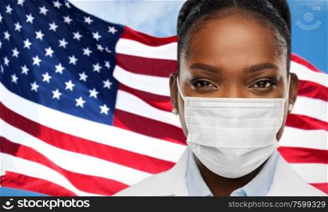 health, medicine and pandemic concept - close up of african american female doctor or scientist in protective medical mask over flag background. african american doctor in medical mask