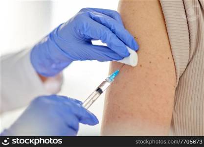 health, medicine and pandemic concept - close up of doctor or nurse with syringe vaccinating patient at hospital. close up of hand with syringe vaccinating patient