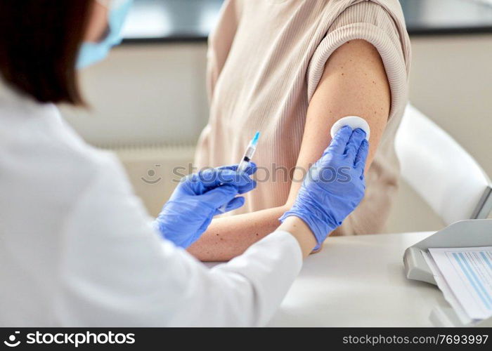 health, medicine and pandemic concept - close up of female doctor or nurse wearing protective medical gloves with syringe vaccinating patient at hospital. female doctor with syringe vaccinating patient