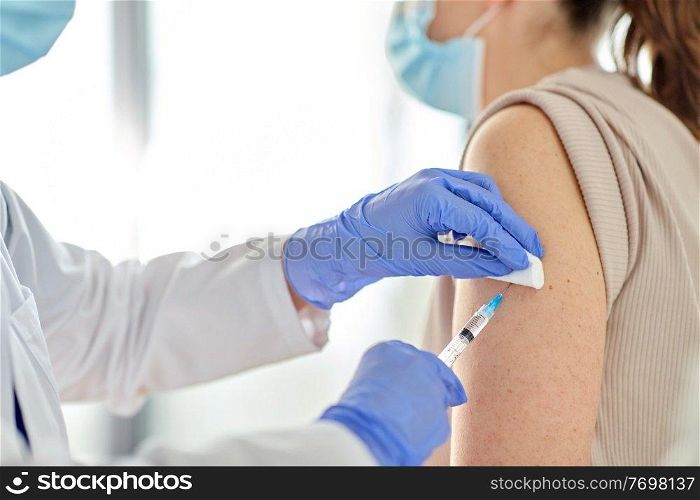 health, medicine and pandemic concept - close up of female doctor or nurse wearing protective medical gloves with syringe vaccinating patient at hospital. female doctor with syringe vaccinating patient
