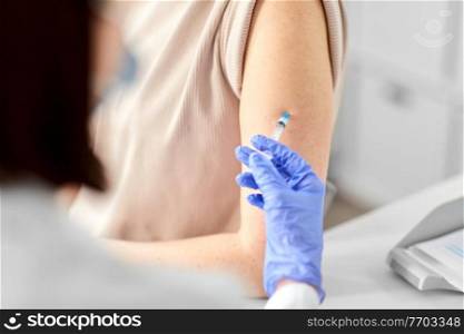 health, medicine and pandemic concept - close up of female doctor or nurse wearing protective medical gloves with syringe vaccinating patient at hospital. female doctor with syringe vaccinating patient