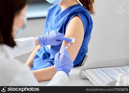 health, medicine and pandemic concept - close up of female doctor or nurse wearing protective medical mask and gloves with syringe vaccinating medical worker hospital. doctor with syringe vaccinating medical worker