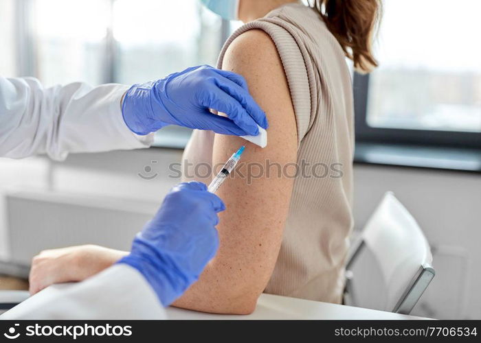 health, medicine and pandemic concept - close up of female doctor or nurse wearing protective medical gloves with syringe vaccinating patient at hospital. female doctor with syringe vaccinating patient