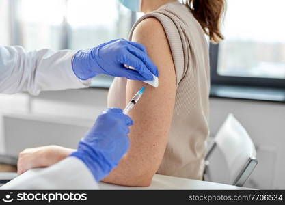 health, medicine and pandemic concept - close up of female doctor or nurse wearing protective medical gloves with syringe vaccinating patient at hospital. female doctor with syringe vaccinating patient