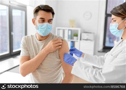 health, medicine and pandemic concept - female doctor or nurse in protective medical mask and gloves sticking patch to patient’s hand after vaccination at hospital. doctor applies patch to patient’s hand at hospital