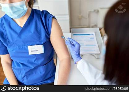 health, medicine and pandemic concept - female doctor or nurse wearing protective mask with syringe vaccinating medical worker hospital. doctor with syringe vaccinating medical worker