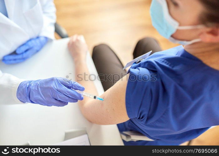 health, medicine and pandemic concept - female doctor or nurse wearing protective mask with syringe vaccinating medical worker hospital. doctor with syringe vaccinating medical worker