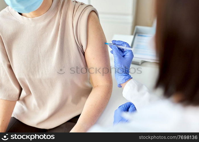 health, medicine and pandemic concept - female doctor or nurse wearing protective medical mask with syringe vaccinating patient at hospital. female doctor with syringe vaccinating patient