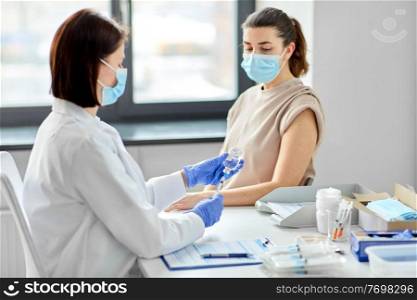 health, medicine and pandemic concept - female doctor or nurse wearing protective medical mask with syringe vaccinating patient at hospital. female doctor with syringe vaccinating patient