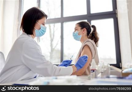 health, medicine and pandemic concept - female doctor or nurse wearing protective medical mask with syringe vaccinating patient at hospital. female doctor with syringe vaccinating patient