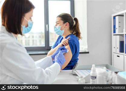 health, medicine and pandemic concept - female doctor or nurse wearing protective medical mask and gloves with syringe vaccinating medical worker hospital. doctor with syringe vaccinating medical worker