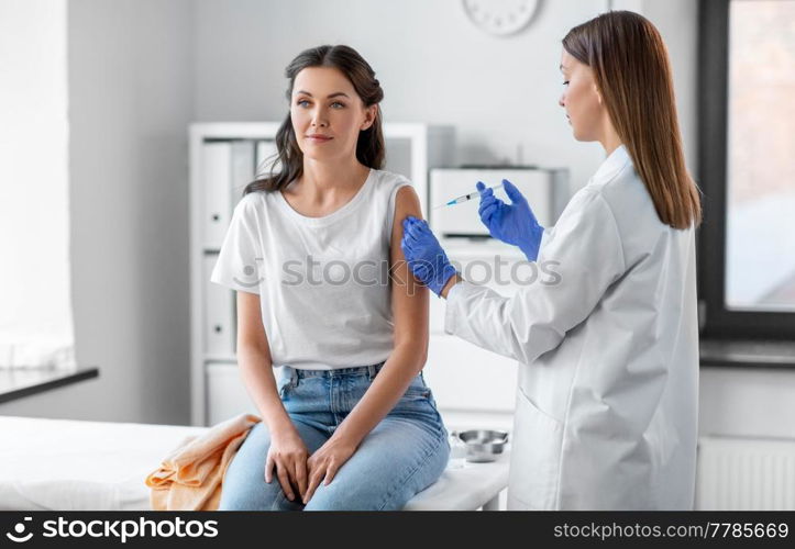 health, medicine and pandemic concept - female doctor or nurse wearing protective medical gloves with syringe vaccinating patient at hospital. female doctor with syringe vaccinating patient