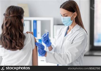 health, medicine and pandemic concept - female doctor or nurse wearing protective medical mask and gloves with syringe vaccinating patient at hospital. female doctor with syringe vaccinating patient