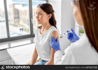 health, medicine and pandemic concept - female doctor or nurse wearing protective medical gloves with syringe vaccinating patient at hospital. female doctor with syringe vaccinating patient