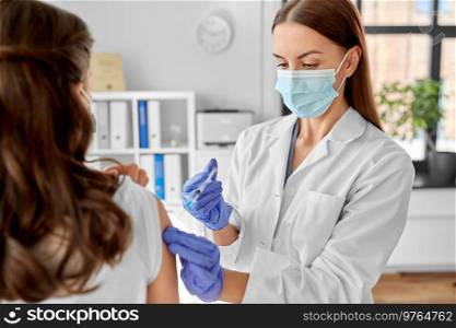 health, medicine and pandemic concept - female doctor or nurse wearing protective medical mask and gloves with syringe vaccinating patient at hospital. female doctor with syringe vaccinating patient