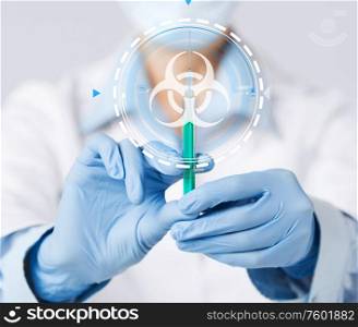 health, medicine and pandemic concept - female doctor&rsquo;s hands in protective medical gloves holding syringe over biohazard caution symbol. hands in gloves with syringe and biohazard sign