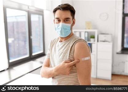 health, medicine and pandemic concept - happy male patient in mask showing patch on his arm after vaccination at hospital. male patient in mask with patch after vaccination