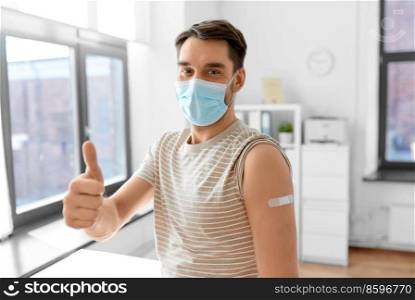 health, medicine and pandemic concept - happy male patient in mask with patch on his arm after vaccination showing thumbs up gesture at hospital. male patient in mask with patch after vaccination