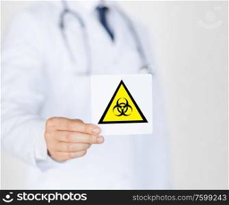 health, medicine and pandemic concept - male doctor holding boihazard caution sign. male doctor holding boihazard caution sign