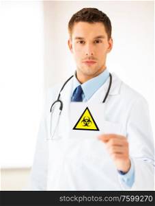 health, medicine and pandemic concept - male doctor holding boihazard caution sign. male doctor holding boihazard caution sign