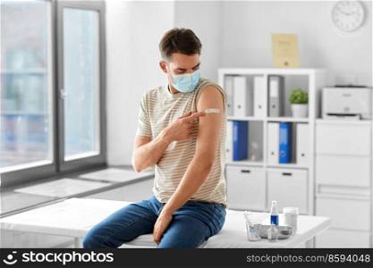 health, medicine and pandemic concept - male patient in mask showing patch on his arm after vaccination at hospital. male patient in mask with patch after vaccination