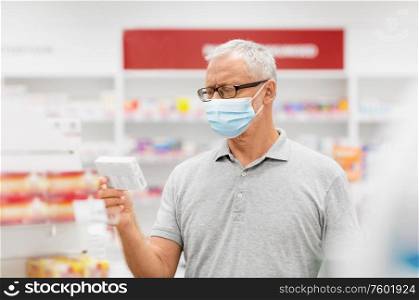 health, medicine and pandemic concept - senior male customer wearing protective medical mask for protection from virus with drug at pharmacy. senior man in medical mask with drug at pharmacy