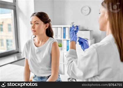 health, medicine and pandemic concept - smiling female doctor or nurse wearing protective medical gloves with syringe vaccinating patient at hospital. female doctor with syringe vaccinating patient