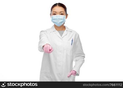 health, medicine and pandemic concept - young asian female doctor or scientist wearing face protective medical mask for protection from virus disease pointing finger to you. asian female doctor in mask pointing finger to you