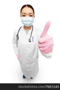 health, medicine and pandemic concept - young asian female doctor with stethoscope wearing face protective medical mask and gloves for protection from virus disease showing thumbs up. asian female doctor in mask showing thumbs up