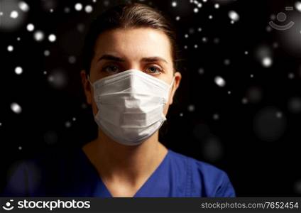 health, medicine and pandemic concept - young female doctor or nurse wearing face protective mask for protection from virus disease over snow on black background in winter. female doctor or nurse in medical face mask