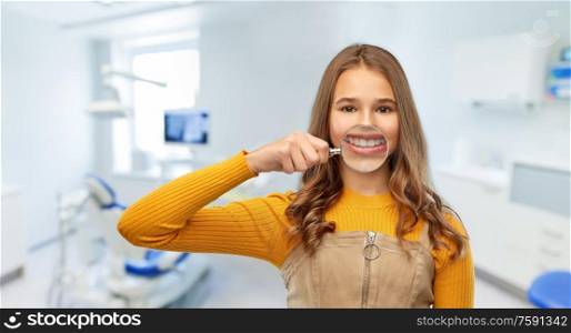 health, medicine and people concept - happy teenage girl showing her teeth through magnifying glass over dental clinic background. girl with magnifier shows teeth at dental clinic